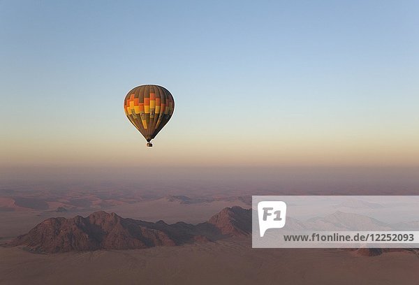 Heißluftballon über einer trockenen Ebene und einsamen Bergrücken bei Tagesanbruch Namib-Wüste Luftaufnahme NamibRand Nature Reserve Namibia Afrika