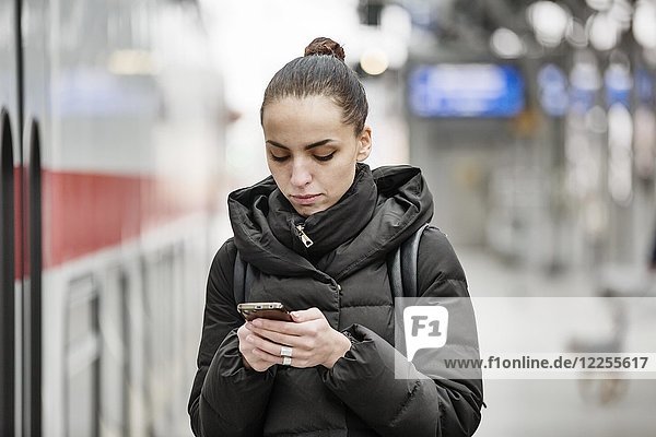Junge Frau auf einem Bahnsteig im Hauptbahnhof schaut auf ihr Smartphone  Köln  Nordrhein-Westfalen  Deutschland  Europa