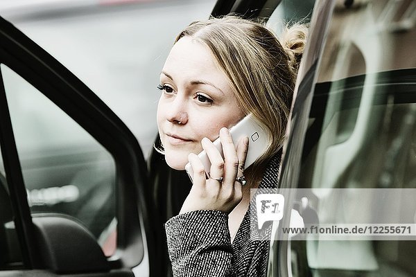 Junge Frau sitzt an einer offenen Tür mit ihrem Smartphone im Auto  Deutschland  Europa