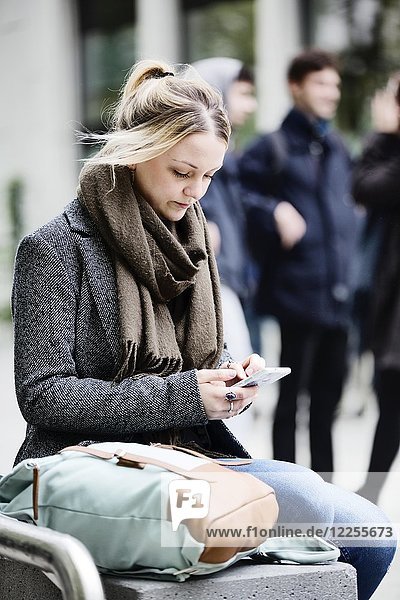 Junge Frau  Studentin  sitzt auf dem Campus mit ihrem Smartphone  Köln  Nordrhein-Westfalen  Deutschland  Europa