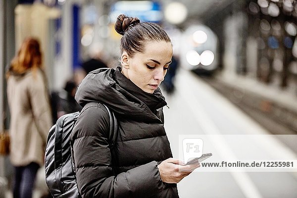 Junge Frau auf einem Bahnsteig im Hauptbahnhof schaut auf ihr Smartphone  Köln  Nordrhein-Westfalen  Deutschland  Europa