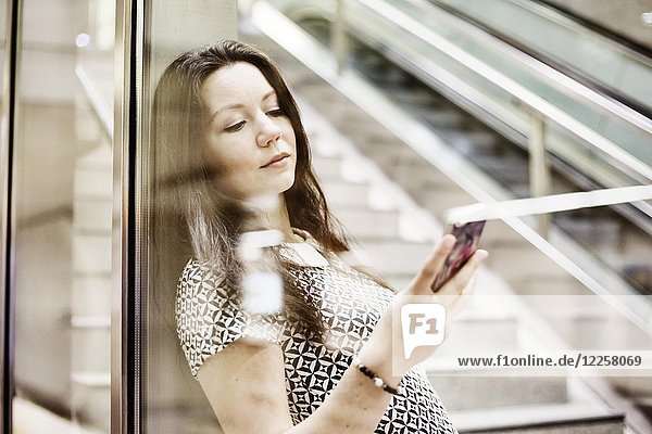 Young woman posing with smartphone behind a glass wall in a subway station  Cologne  North Rhine-Westphalia  Germany  Europe
