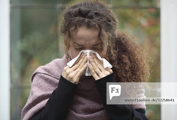 Symbolbild Erkältung Grippe Krankheit Portrait einer Frau beim Nase putzen mit Papiertaschentuch