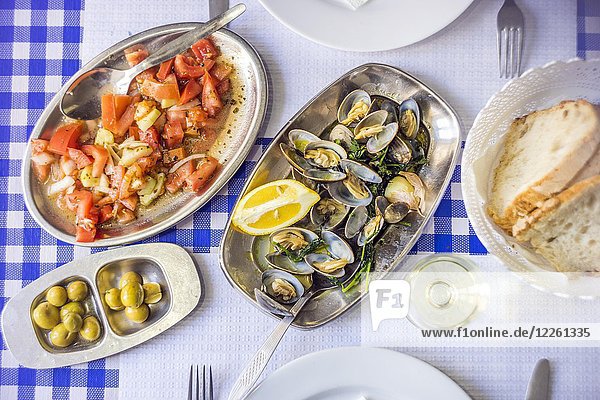 Covered table with delicious clams served on silverware  white wine  tomato salad  bread and olives from above  Portugal  Europe
