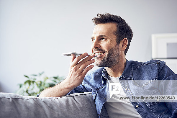 Smiling man sitting on sofa using cell phone
