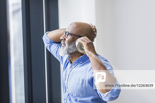 Businessman looking out of window while using tin can phone