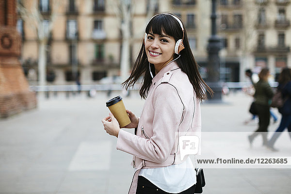 Spanien  Barcelona  lächelnde Frau mit Kaffee und Kopfhörer in der Stadt