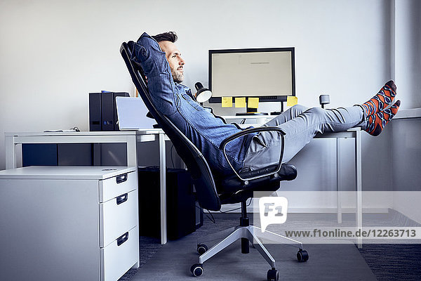 Mann sitzt am Schreibtisch und entspannt im Büro