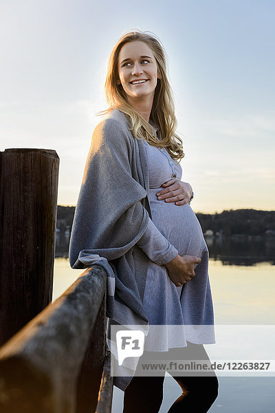 Smiling pregnant woman standing at lakeshore