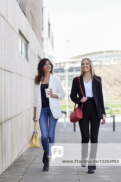 Zwei entspannte Geschäftsfrauen mit Handtaschen und Kaffee zum Spazierengehen auf dem Bürgersteig