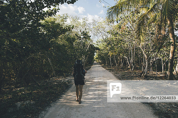 Kuba  Cienaga de Zapata  Junge Frau mit Rucksack  die auf einer von Bäumen gesäumten Straße läuft.