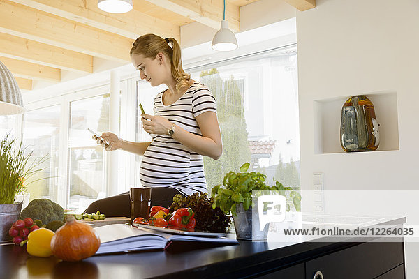 Schwangere Frau in der Küche zu Hause mit dem Handy