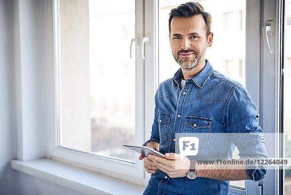 Portrait of smiling man holding tablet at the window