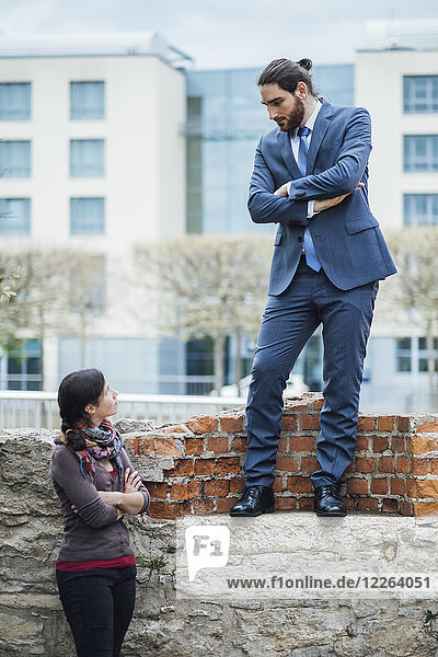 Businessman standing on a wall looking down at woman