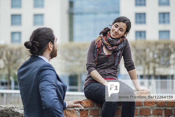 Woman sitting on a wall outside office building smiling at businessman