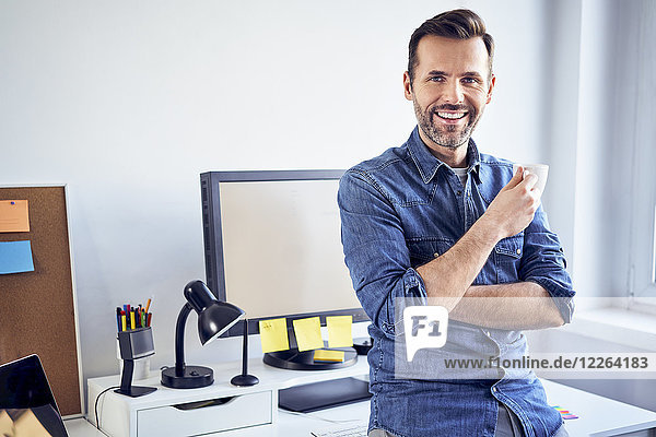 Portrait of smiling man with cup of coffee at desk in office