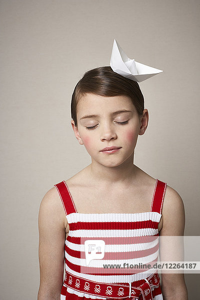 Porträt des kleinen Mädchens mit Papierboot auf dem Kopf