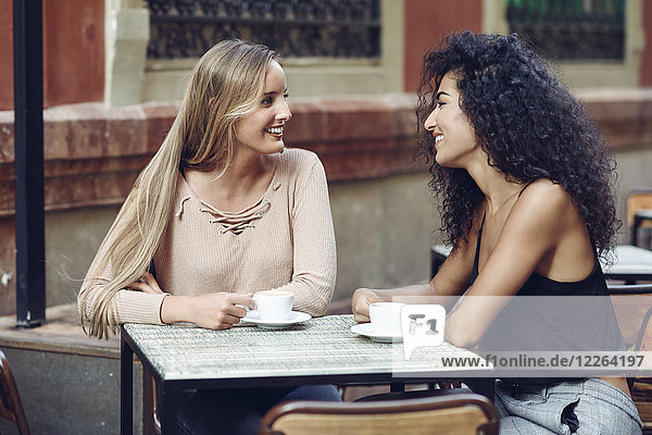 Two friends drinking coffee in sidewalk cafe