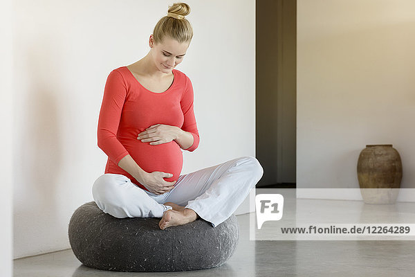 Lächelnde schwangere Frau  die zu Hause auf einem Puff sitzt.