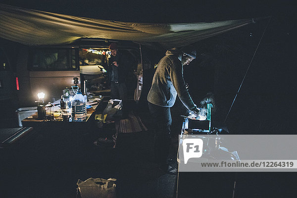 Canada  British Columbia  two men cooking under tarp at minivan at night
