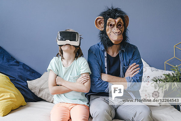 Father wearing monkey mask sitting next to son wearing VR glasses at home