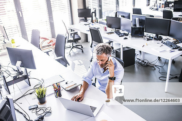 Reife Geschäftsleute sitzen am Schreibtisch im Büro mit Handy und Laptop