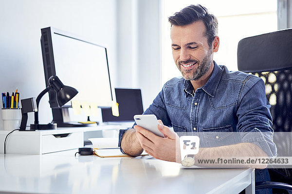 Smiling man using cell phone at desk in office