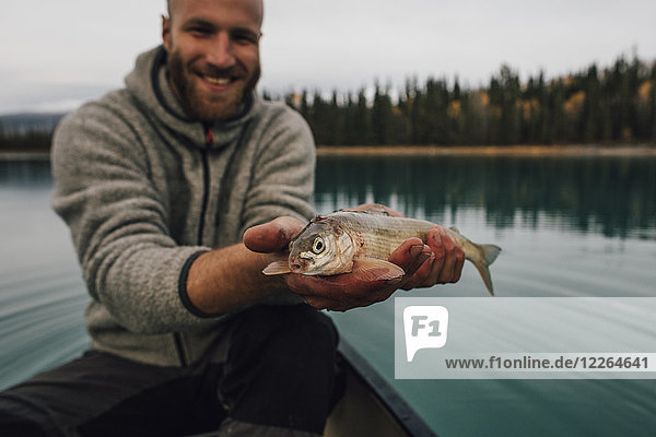 Kanada  British Columbia  Porträt eines lächelnden Mannes im Kanu mit Fisch auf dem Boya Lake