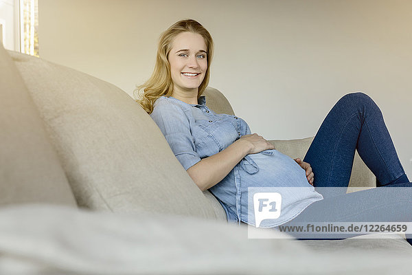 Portrait of smiling pregnant woman sitting on couch at home