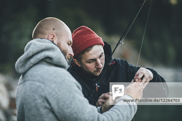 Young man helping friend with fishing rod