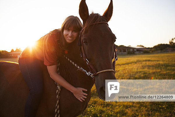 Porträt einer lächelnden Frau auf einem Pferd bei Sonnenuntergang