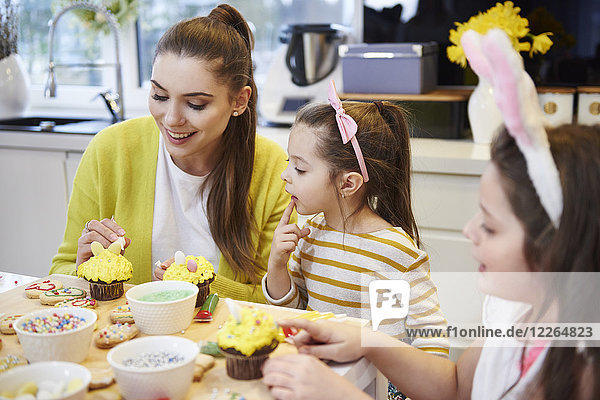 Mother with daughters decorating Easter cookies and muffins in kitchen