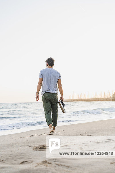 Back view of man walking barefoot on the beach