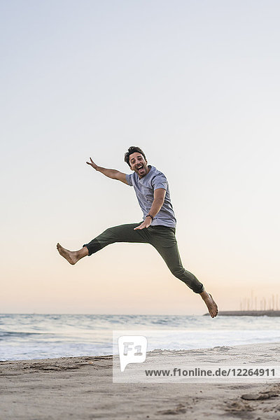 Happy young man jumping in the air on the beach at sunset