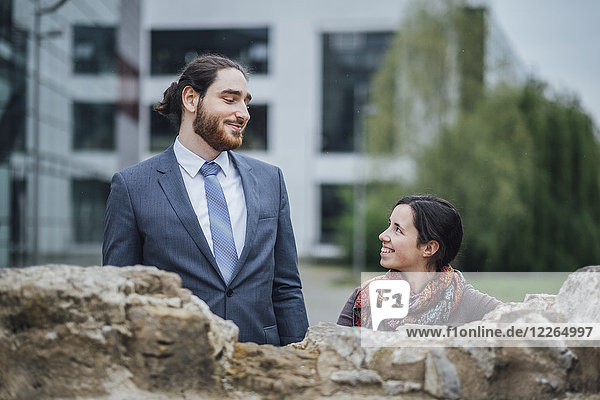 Smiling businessman and woman behind a wall outside office building