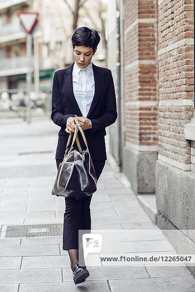 Portrait of young businesswoman with bag walking on pavement