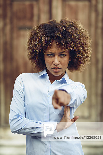 Porträt einer ernsthaften Frau mit Afro-Frisur,  die mit dem Finger nach draußen zeigt.