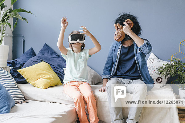 Father wearing monkey mask looking at son wearing VR glasses at home