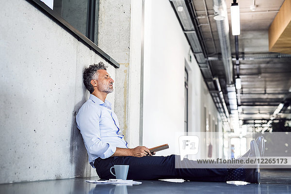 Mature businessman sitting on the floor leaning against the wall
