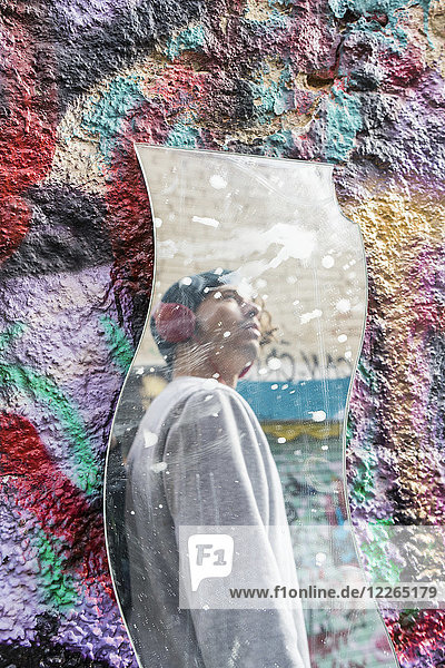 Spiegelbild eines jungen Mannes mit Kopfhörer beim Betrachten von Graffiti
