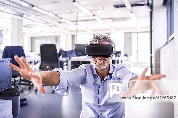 Happy mature businessman wearing VR glasses in office