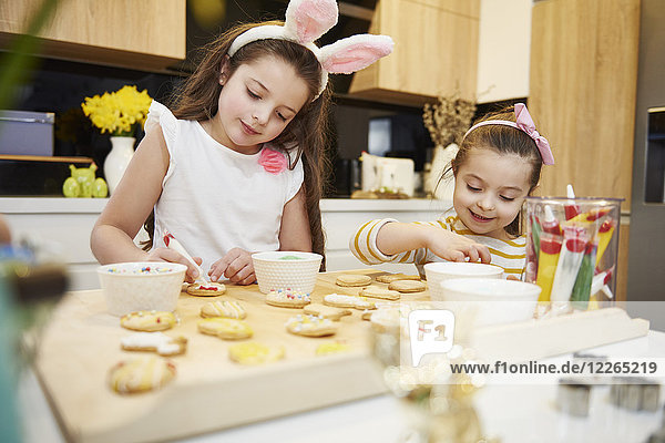 Sisters decorating Easter cookies in kitchen