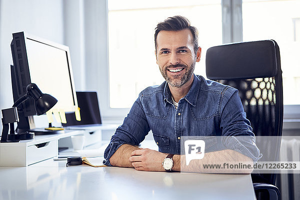 Porträt eines lächelnden Mannes am Schreibtisch im Büro