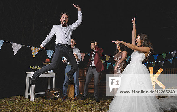 Überraschte Braut schaut auf einen Mann  der mit Freunden auf einer Nachtfeldparty springt.