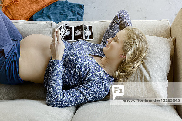 Smiling pregnant woman lying on couch looking at ultrasound images