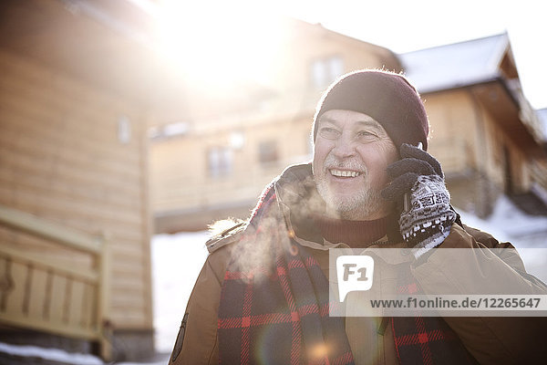 Lächelnder älterer Mann beim Telefonieren im Bergdorf im Winter