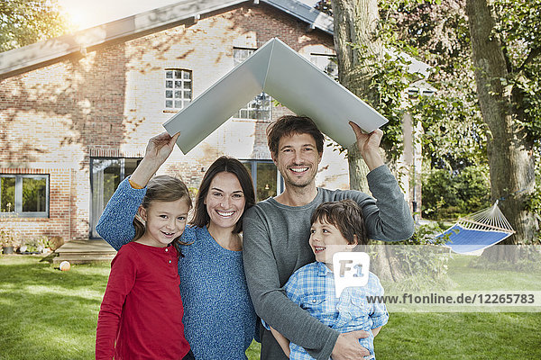 Portrait of happy family in garden of their home holding roof
