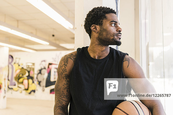 Man with tattoos holding basketball looking away
