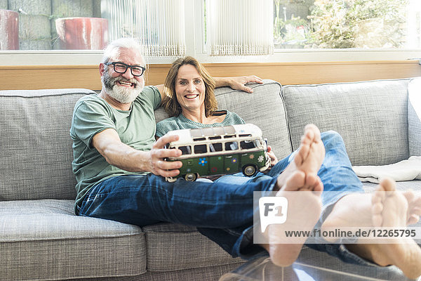 Glückliches reifes Paar auf der Couch zu Hause mit Minibusmodell