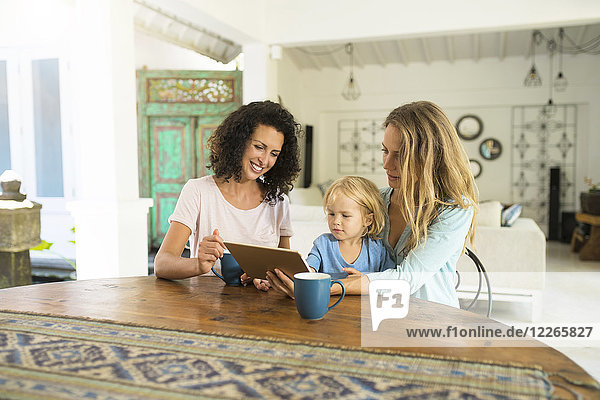 Two women with a child looking at tablet at kitchen table